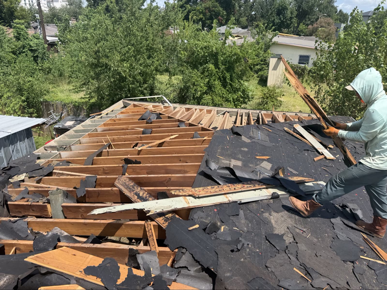 Bright Roofing crew member tearing up rotted roof decking in Houston, rafters exposed